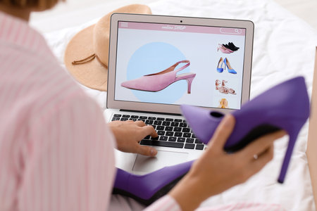 Young woman with new shoes using laptop in bedroom, closeup. online shoppingの写真素材