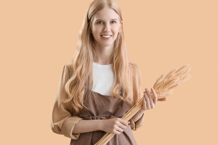 Young woman with wheat ears on beige backgroundの写真素材