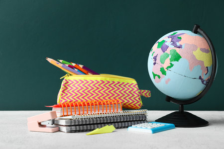 Pencil case with school stationery and globe on table against green background