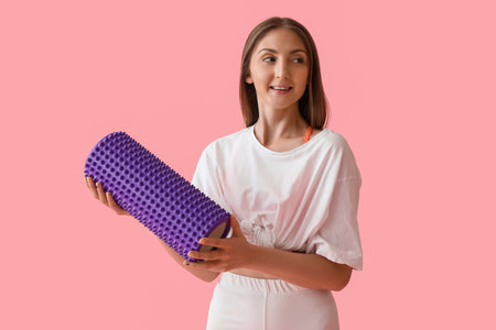 Young woman with foam roller on pink background