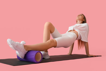 Young woman training with foam roller on pink backgroundの写真素材