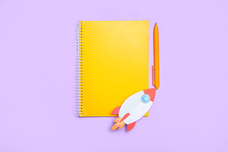 Paper rocket with notebook and pen on violet backgroundの写真素材