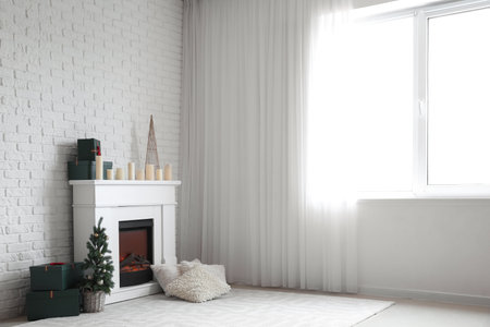 Electric fireplace with candles, gift boxes and Christmas tree near white brick wallの写真素材