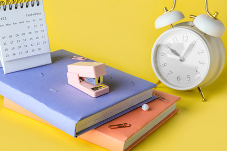 Stapler with books, alarm clock and calendar on yellow background, closeupの写真素材