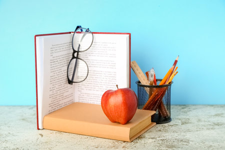 School stationery with apple and eyeglasses on table against blue backgroundの写真素材