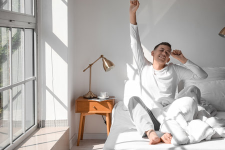 Handsome young man stretching on bed at homeの写真素材