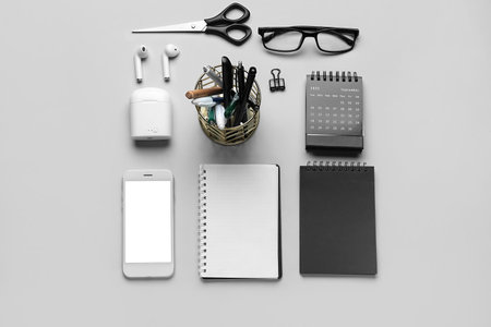 Set of stationery with eyeglasses, mobile phone and earphones on light background