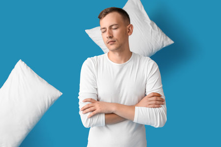 Young man and pillows on blue backgroundの写真素材