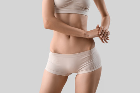 Slim young woman in underwear on light backgroundの写真素材