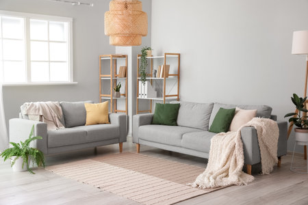 Interior of light living room with gray sofas, shelving units and houseplants