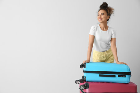 Female African-American tourist with suitcases on light backgroundの写真素材