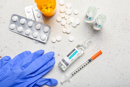 Ampules of monkeypox vaccine with syringe, pills and gloves on light background