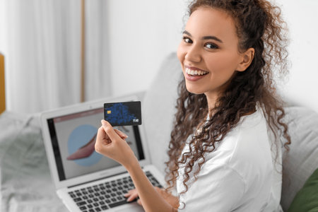 Young African-American woman with credit card and laptop shopping online at home, closeup
