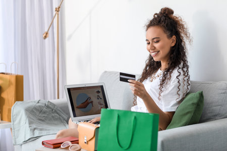 Young African-American woman with credit card and laptop shopping online at homeの写真素材