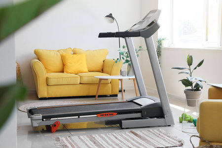 Interior of light living room with treadmill and yellow sofa