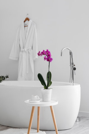 Orchid flower and cup on table near bathtubの写真素材