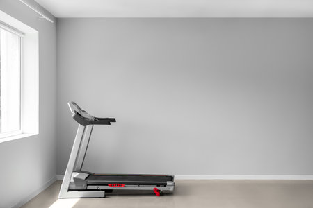 Modern treadmill near light wall in room