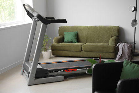 Interior of light living room with treadmill and sofa
