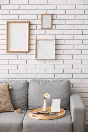 Tray with peony flower, blank photo frame and magazine on sofa near white brick wallの写真素材