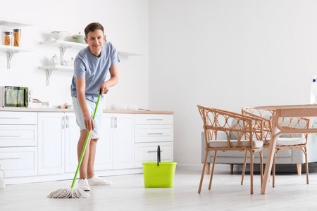 Handsome young man mopping floor in modern kitchenの写真素材