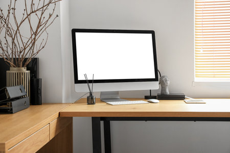 Modern workplace with computer, tablet and tree branches in vase near light wallの写真素材