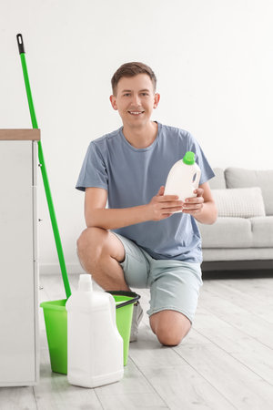 Young man with bottle of detergent in the kitchenの写真素材