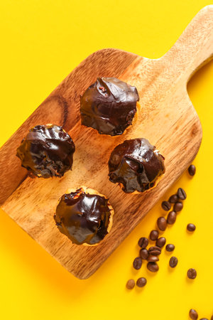 Wooden board with tasty eclairs on yellow background, closeup