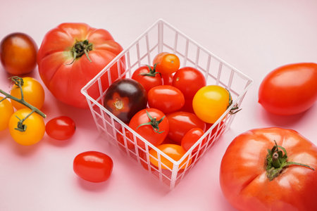 Basket with different fresh tomatoes on pink backgroundの写真素材