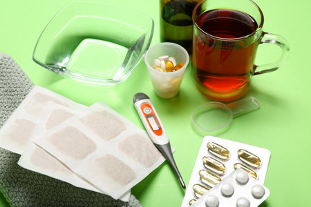 Mustard plasters with medicines, cup of tea and towel on green backgroundの写真素材
