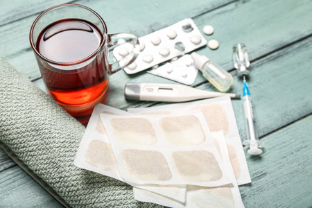 Mustard plasters with medicines, thermometer, cup of tea and towel on color wooden background