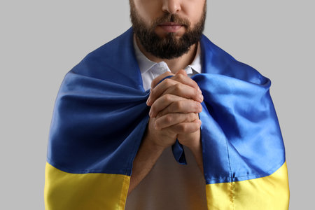 Young man with flag of Ukraine praying on gray background, closeupの写真素材