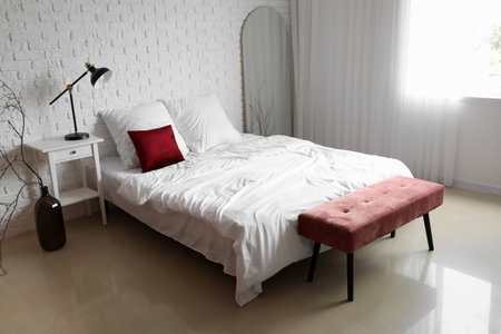 Interior of light room with pink bench, bed and mirror