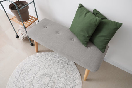 Soft bench with green pillows near light wall