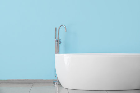 Modern bathtub with tap near color wallの写真素材