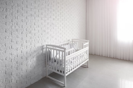 Baby crib with pillows near white brick wallの写真素材