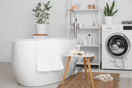Modern bathtub and table with bath accessories in light roomの写真素材