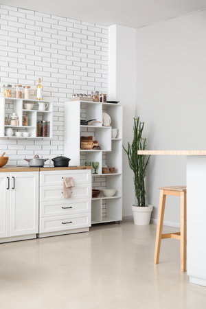 Stylish interior of light kitchen with modern counters and shelf unit near white brick wallの素材 [FY310192231569]