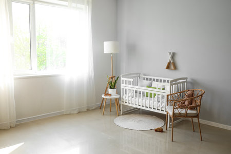 Interior of light nursery with baby crib, lamp, table and armchairの写真素材