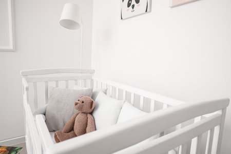 Baby crib with pillows and teddy bear near light wallの写真素材