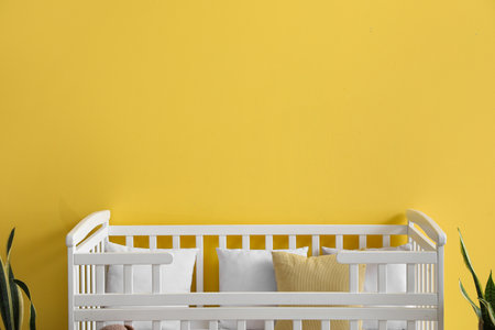 Comfortable crib and houseplants near yellow wall in children's roomの写真素材