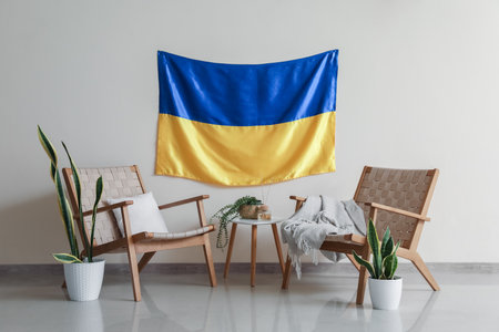 Comfortable armchairs and flag of Ukraine hanging on white wall in light roomの写真素材