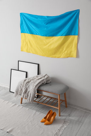 Bench with plaid, blank photo frames and flag of Ukraine hanging on white wallの写真素材