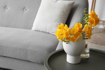 Vase with beautiful flowers and reed diffuser on table near sofaの写真素材