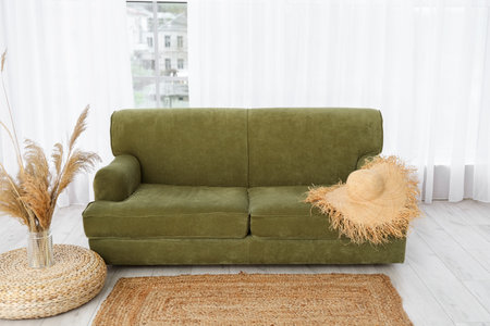 Comfortable sofa, wicker hat and vase with pampas grass near big window in living room