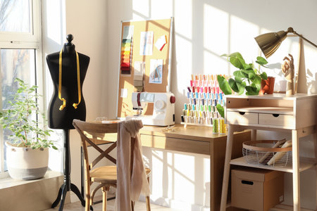 Interior of stylish atelier with tailor's workplace, thread spools and mannequin