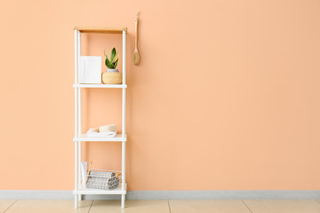 Shelving unit with bath supplies, frame and houseplant near beige wallの写真素材