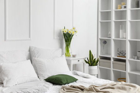 Vase with daffodils and candle on table in light bedroom