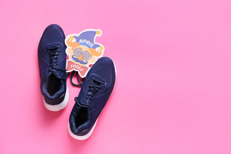 Shoes with tied laces and card with text APRIL FOOL'S on pink background