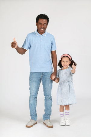 Portrait of little African-American girl and her father showing thumb-up on gray backgroundの写真素材