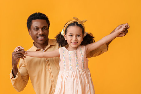 Portrait of little African-American girl and her father on yellow backgroundの写真素材